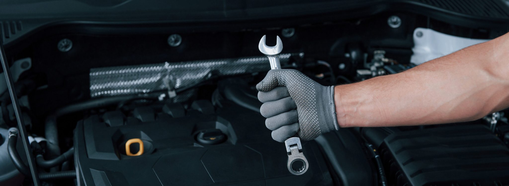 In the shop. Man's hand in glove holds wrench in front of broken automobile.